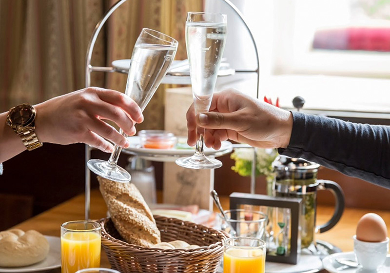 Zwei Personen stoßen mit Sekt bei Frühstück im Kablu an